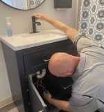 The Werrlein Companies repair person services the plumbing system under a sink.