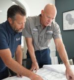 The Werrlein Companies employees plan a plumbing or HVAC solution for a client. Both men are hunched over a table and talk while working on a master plan.